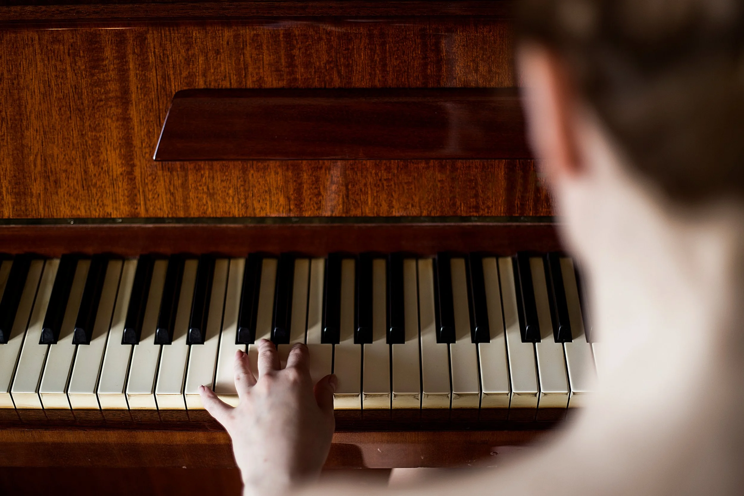 A young child playing the piano, with a close-up of their small hand on the white keys.