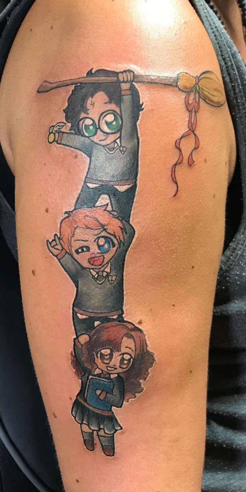 Tatouage de quatre personnages de style chibi, empilés verticalement, avec un balai en haut, trois enfants souriants et faisant des gestes joyeux.