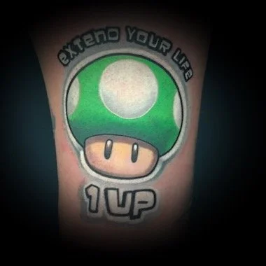 Tatouage d'une pièce de Mario avec le texte 'Extend your life' et '1 UP'.