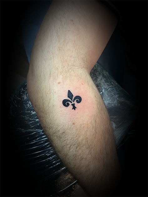 Tatouage d'une fleur de lys stylisée noire sur le bras d'une personne.