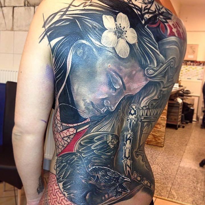 Tatouage coloré couvrant le côté du corps d'une femme, représentant une femme endormie ou pensive avec un grand bouquet de fleurs, un oiseau noir avec la bouche ouverte, et des éléments décoratifs en style réaliste.