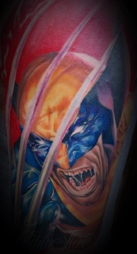 Tatouage d'un personnage avec un visage effrayant ou monstrueux, montrant des dents acérées, dans un style coloré et artistique.