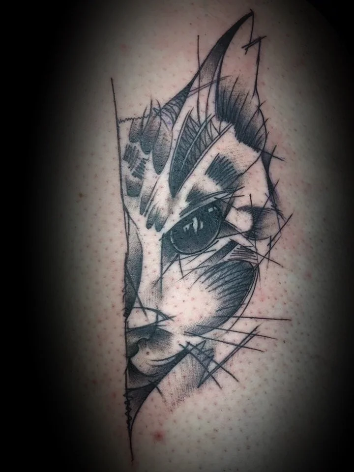 Tatouage en noir et gris d'un visage de chat stylisé avec des détails géométriques et des lignes dynamiques.