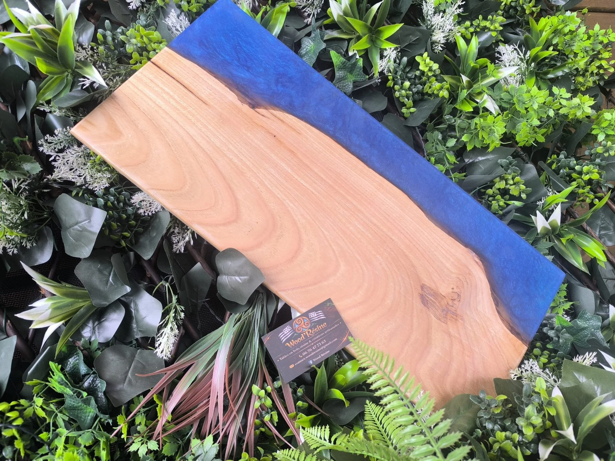 Une table en bois avec un bord peint en bleu, placée parmi des plantes vertes et des feuillages