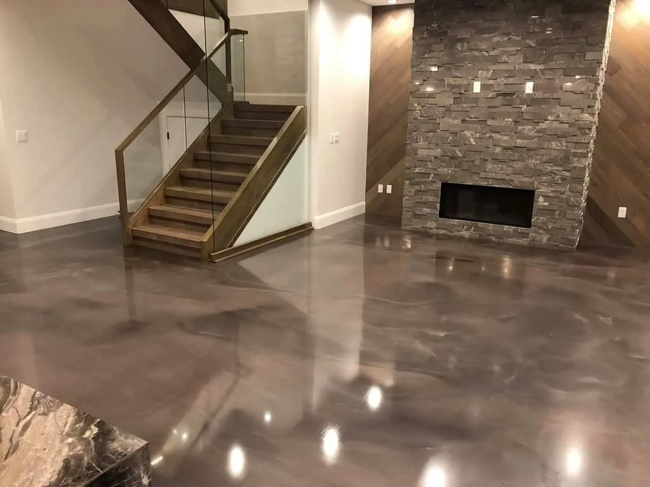 Salon avec plancher en bois poli, cheminée en pierre et escalier en bois avec rampe en verre.