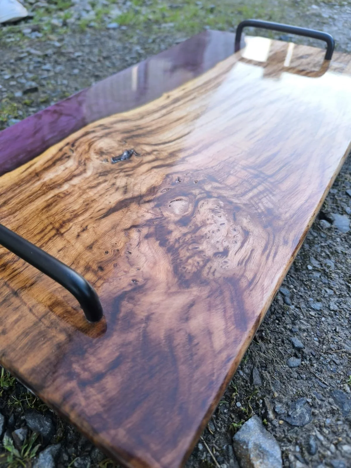 Table en bois avec poignées en métal, posée sur le sol extérieur avec gravures naturelles dans le bois.