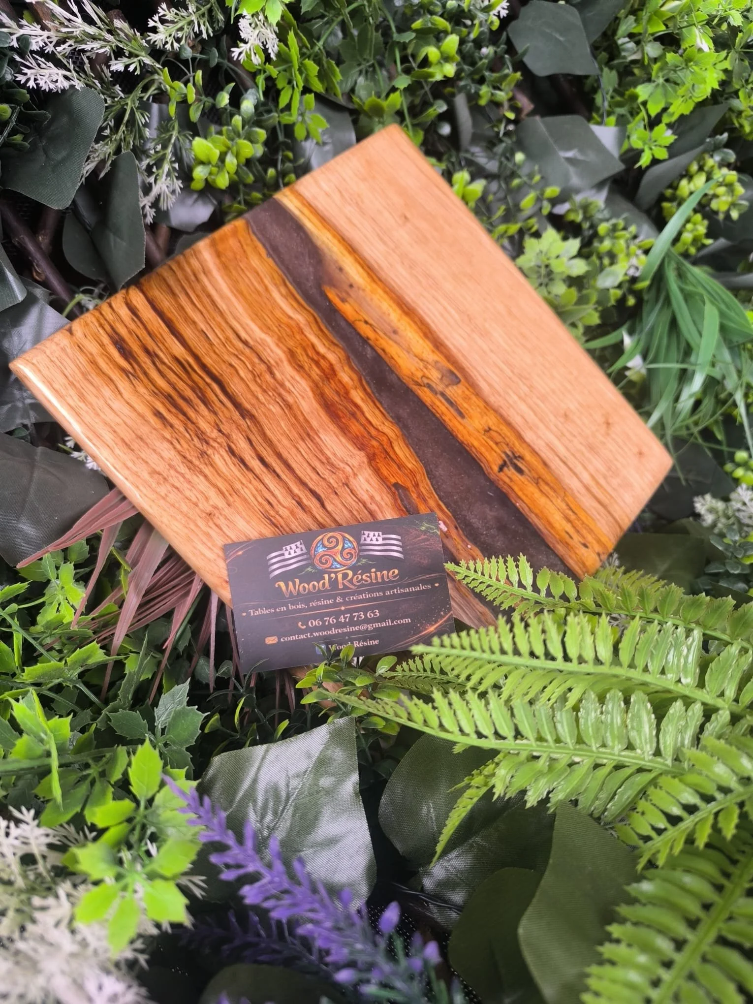 Une table en bois résine avec des teintes naturelles, entourée de feuilles et de plantes vertes.