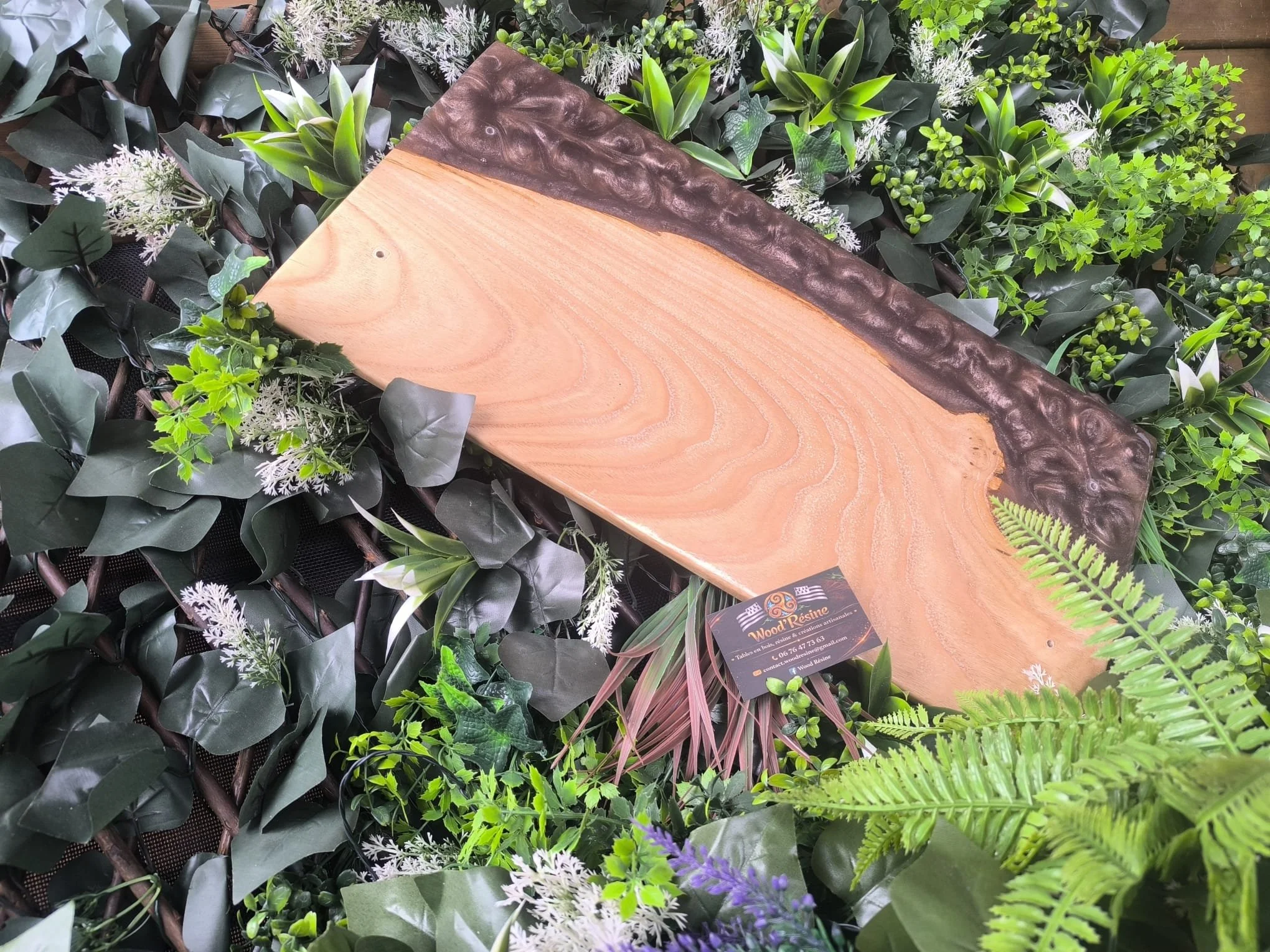Table en bois naturel avec un cadre en bois sculpté entourée de plantes vertes et de fleurs dans une décoration végétale.