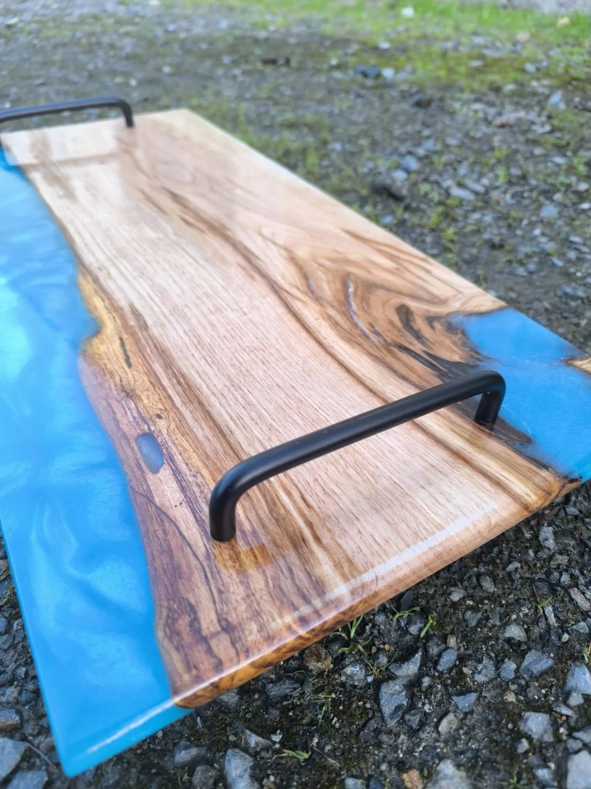 Table en bois avec résine époxy bleue sur les côtés, placée à l'extérieur sur un sol rocheux.