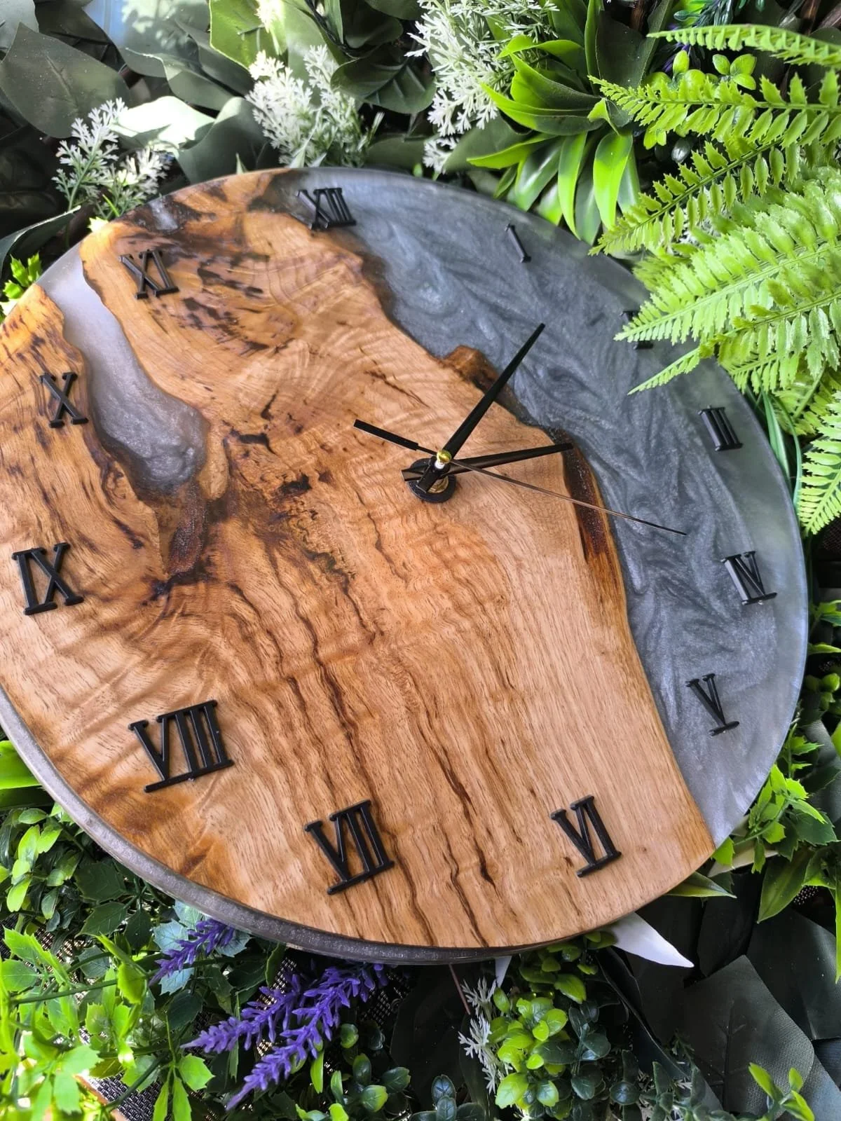 Horloge murale en bois avec une face en bois naturel et une face en résine noire, entourée de plantes vertes.