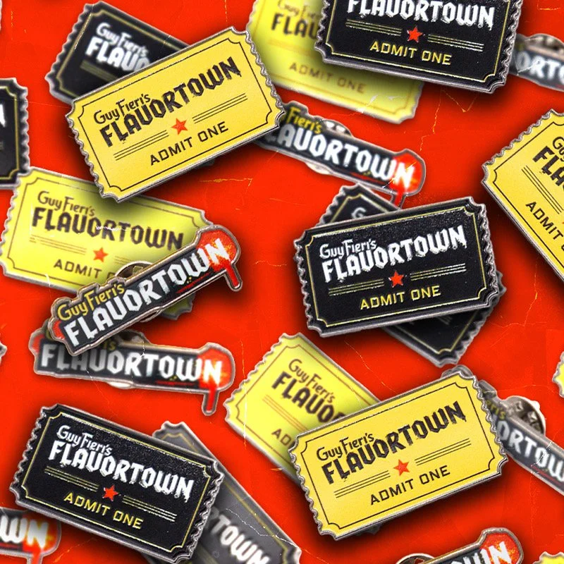 A collection of novelty ticket-shaped badges with the text "Guy Fieri's Flavortown Admit One" in yellow and black colors.
