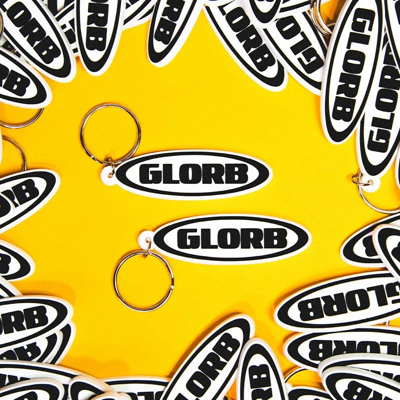 Multiple black and white GLORB stickers and keychains arranged on a yellow background.