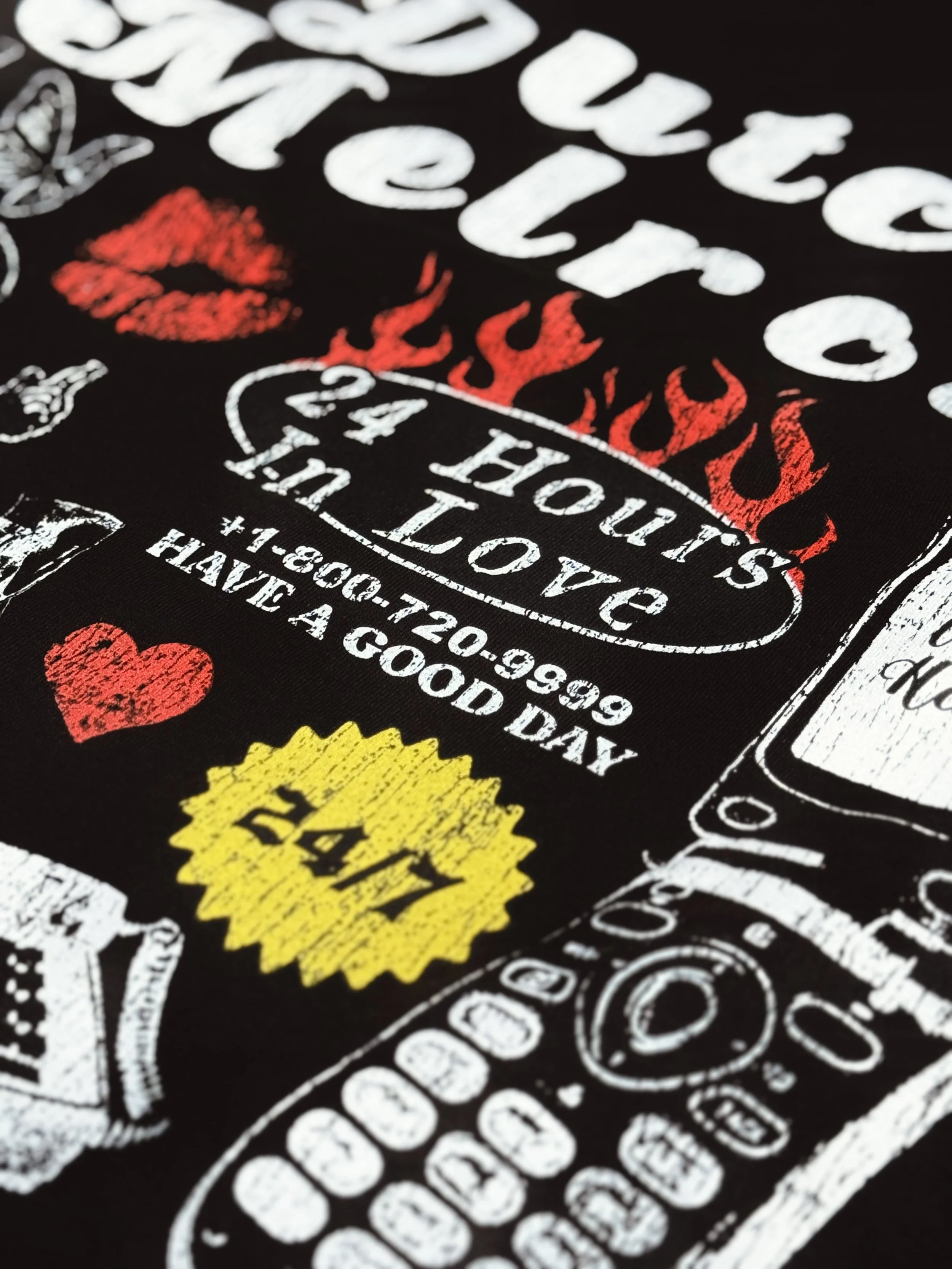 Close-up of a black fabric featuring colorful printed designs, including red lips, red flames, a red heart, a yellow sunburst, and various white text and patterns.