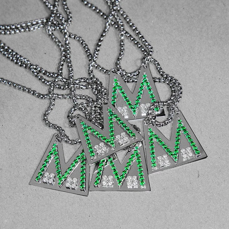 Multiple silver necklaces with rectangular pendants decorated with green and white rhinestones, spelling out 'MOM'.