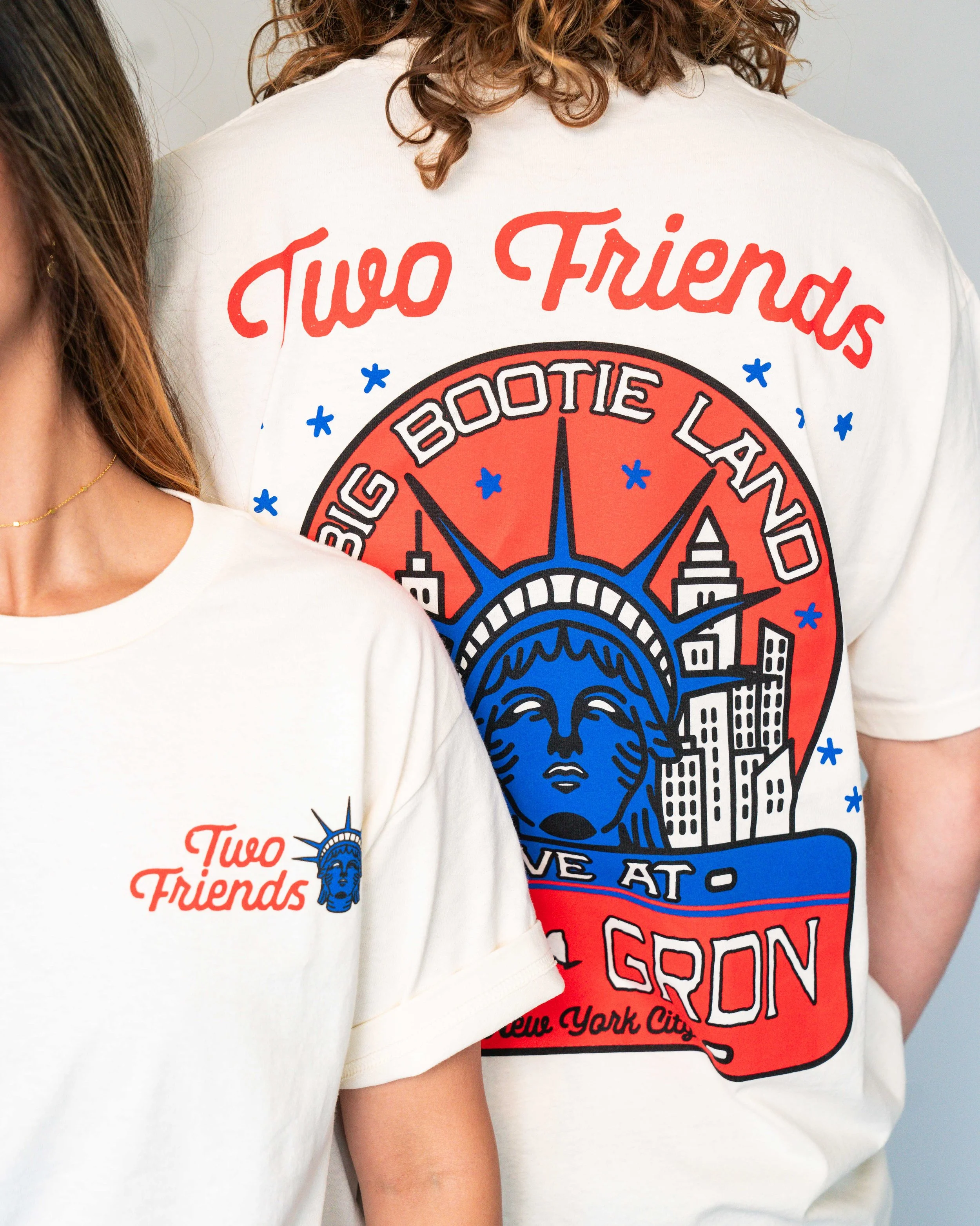 Two women wearing white T-shirts featuring a graphic design with the Statue of Liberty's face and famous New York City landmarks, and the phrase 'Two Friends'.