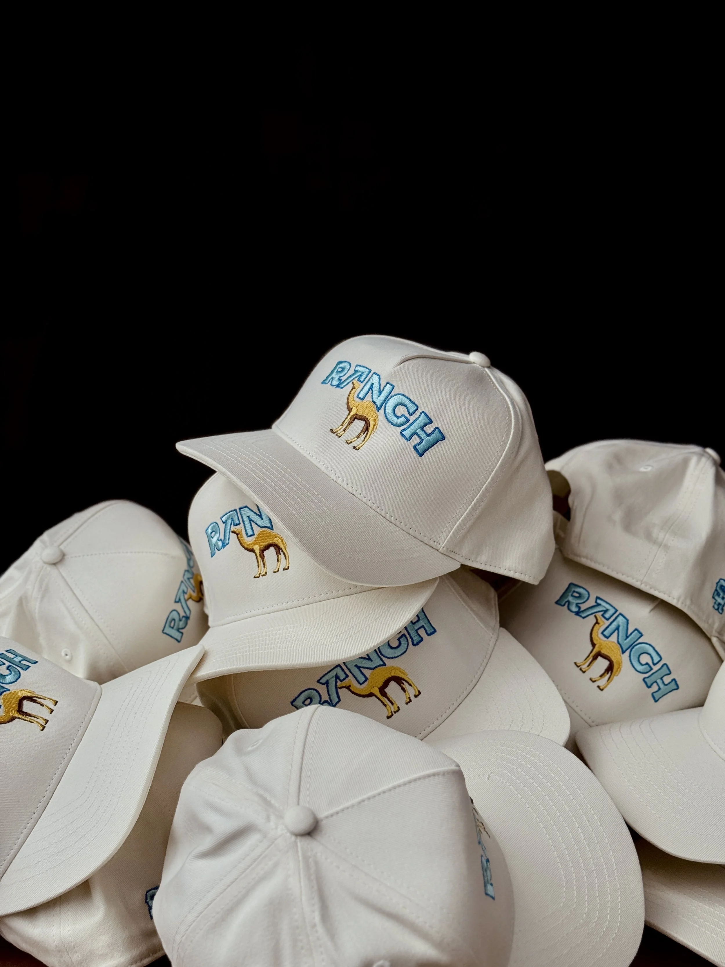 Multiple white baseball caps with embroidered text "RTH" and a camel logo, stacked together against a black background.