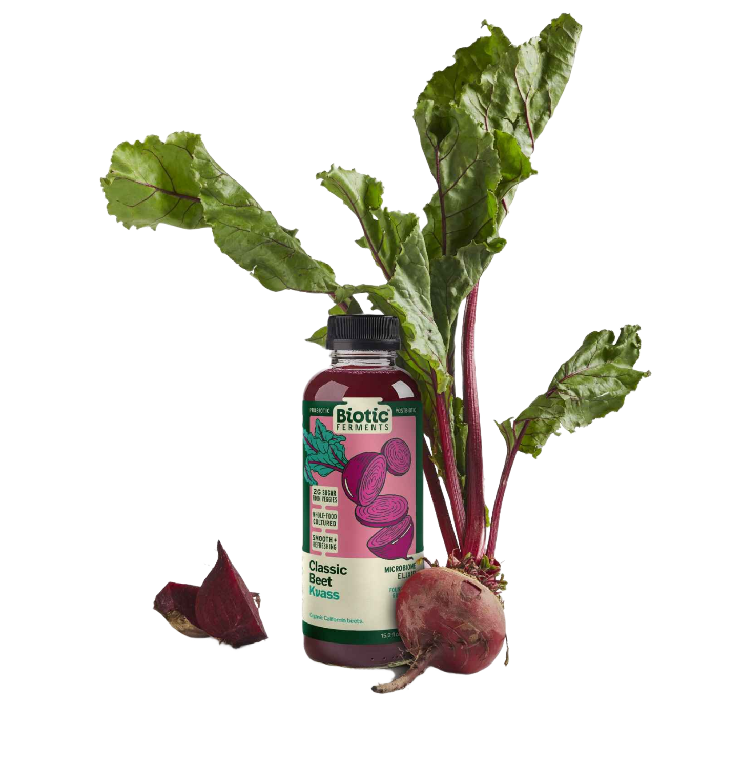 A bottle labeled 'Biotic Ferments Classic Beet Kvass' positioned in front of a fresh beet with leaves attached and one beetroot cut in half, showing its red interior, on a white background.