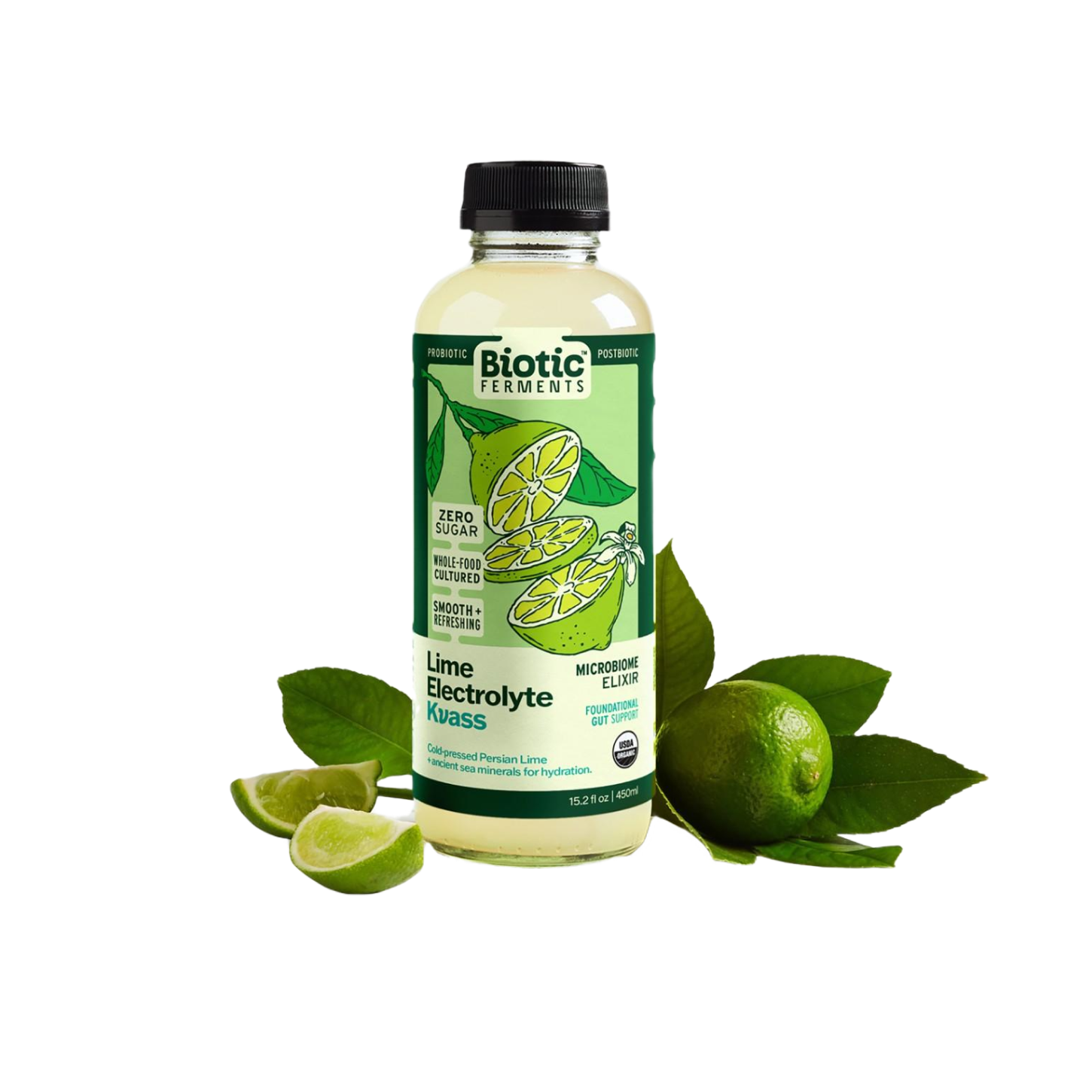 A bottle of Biotic Ferments Lime Electrolyte Kvass with a lemon illustration on the label, placed among fresh limes and lime wedges with green leaves.