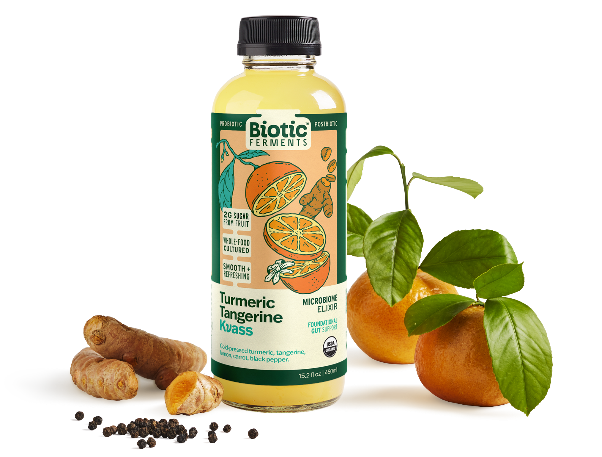 A bottle of Biotic Ferments Turmeric Tangerine Kvass probiotic beverage in front of fresh tangerines with leaves, turmeric roots, black peppercorns, and ginger root on a light background.