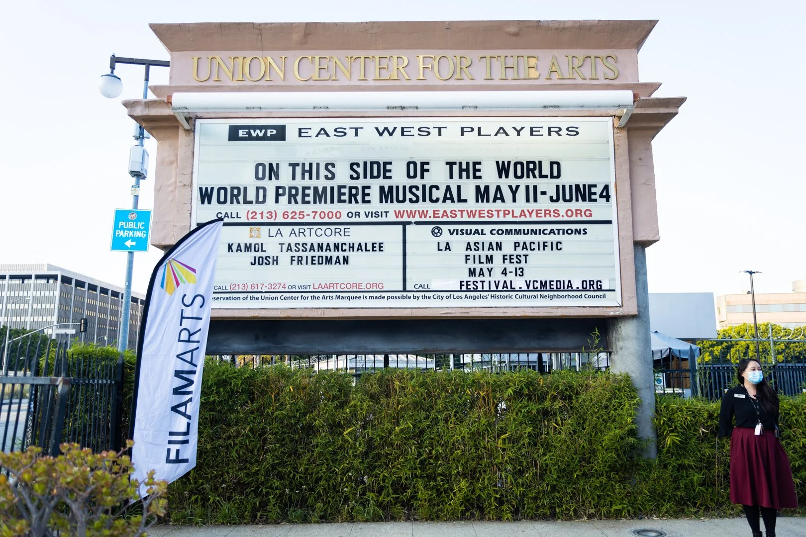 Marquee sign at the Union Center for the Arts advertising the East West Players' world premiere musical, running from May 11 to June 4. The sign includes contact info and event details, with a person wearing a face mask standing nearby.