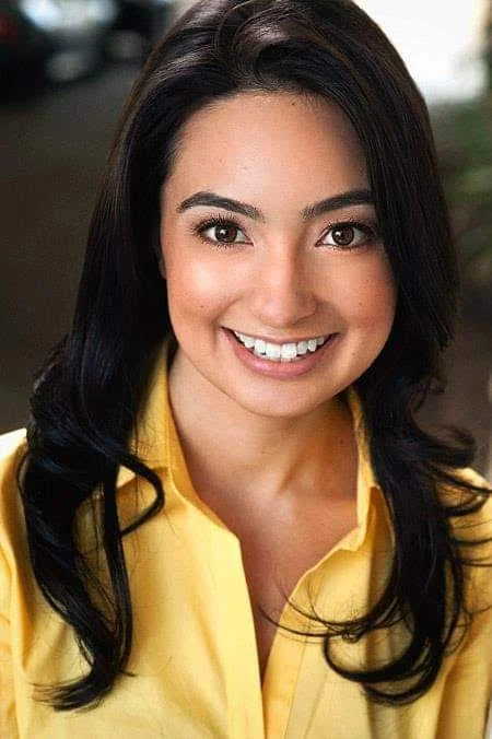 A woman with dark hair smiling outdoors, wearing a yellow blouse.
