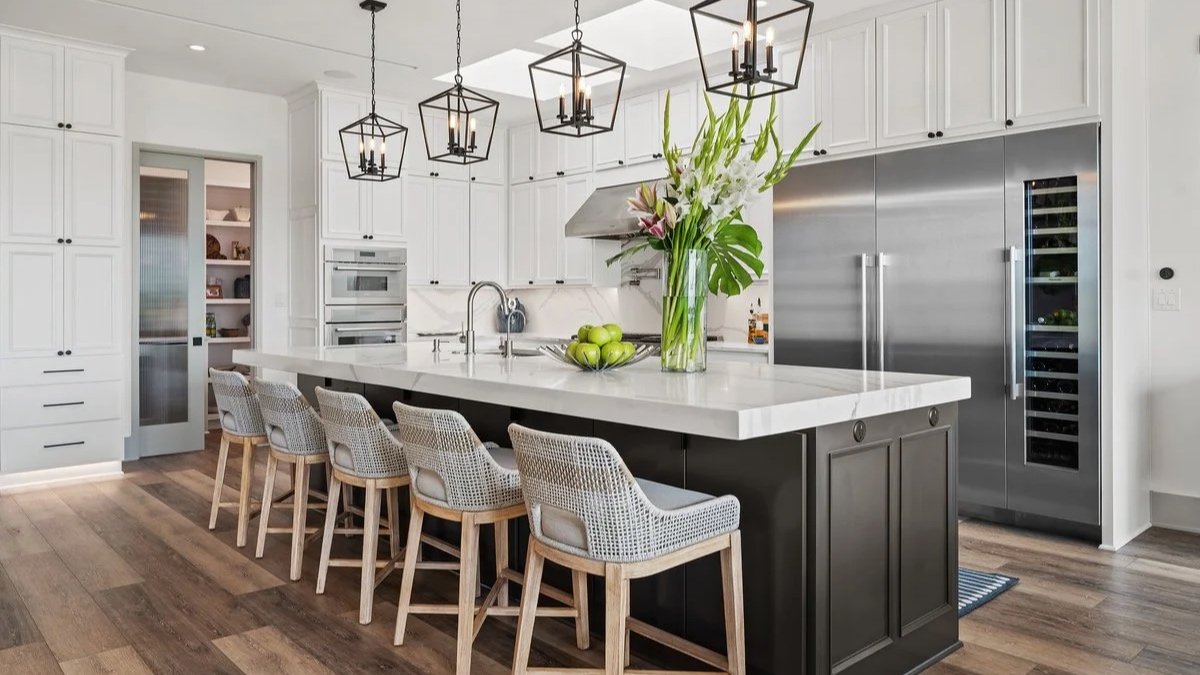 Modern kitchen with a marble island, pendant lights, wooden chairs, and large window overlooking trees, decorated with flowers.