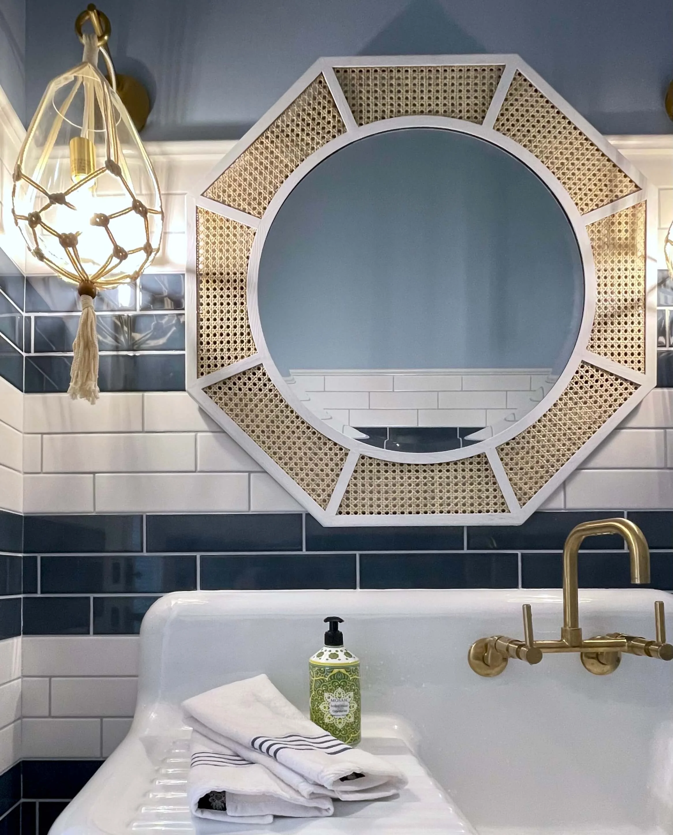 Bathroom with black and white tiled walls, a large decorative mirror, and a gold faucet over a bathtub. Linen towels and a soap dispenser are placed on the side of the tub.