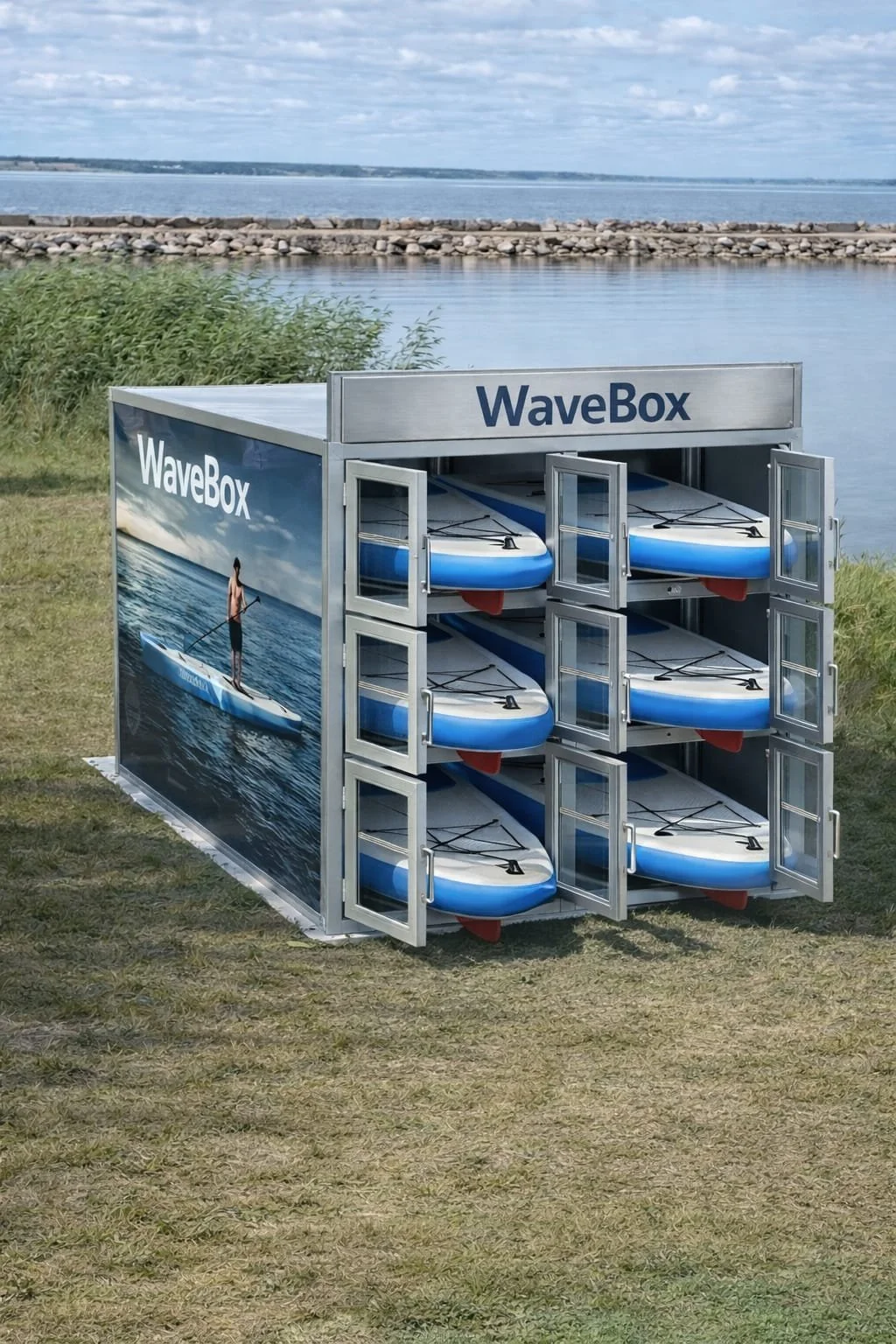 A storage unit labeled 'WaveBox' contains multiple transparent and standard stand-up paddleboards, placed outdoors on the beach near a body of water.