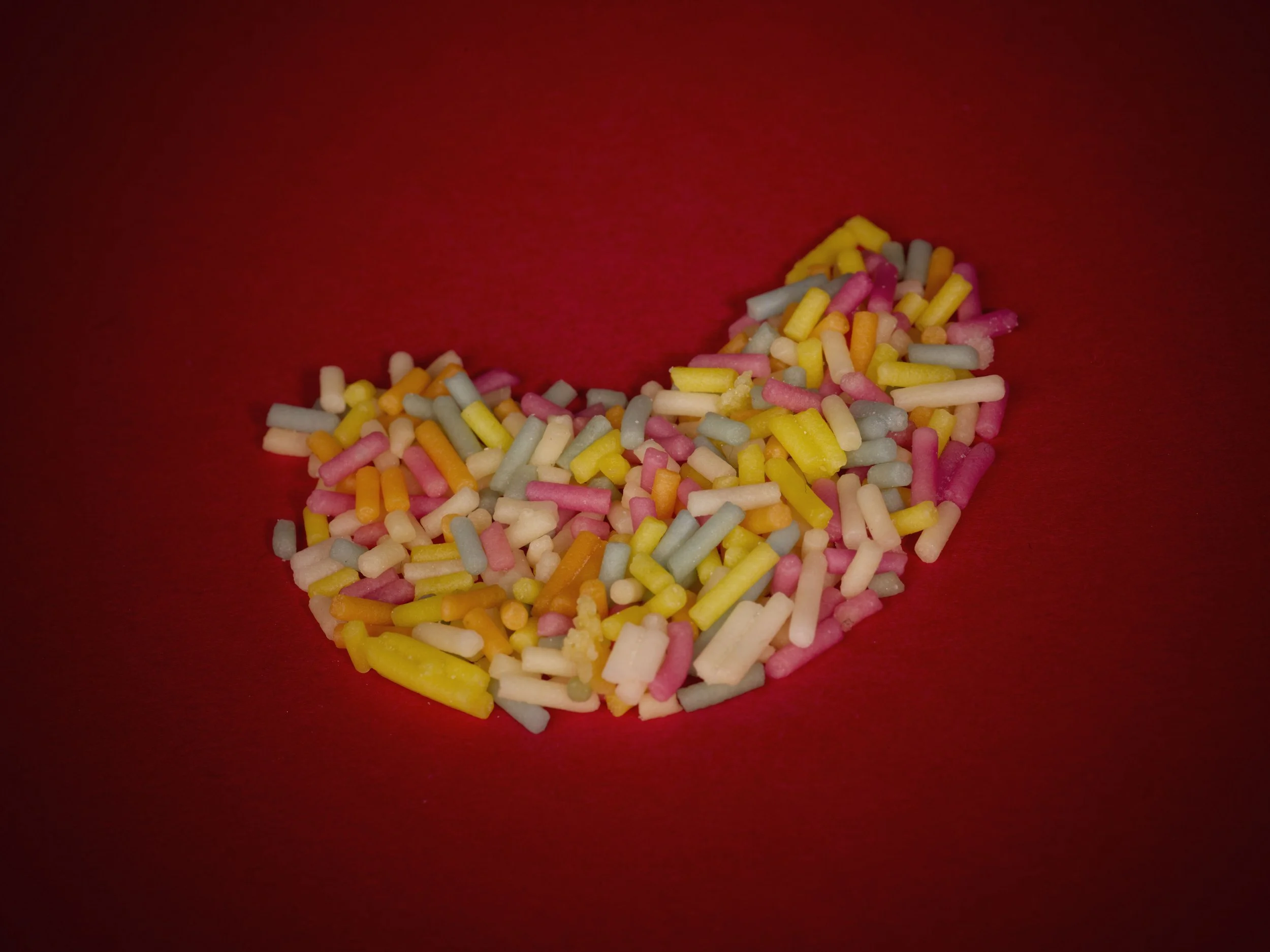 Colorful sprinkles arranged in a heart shape on a red background.