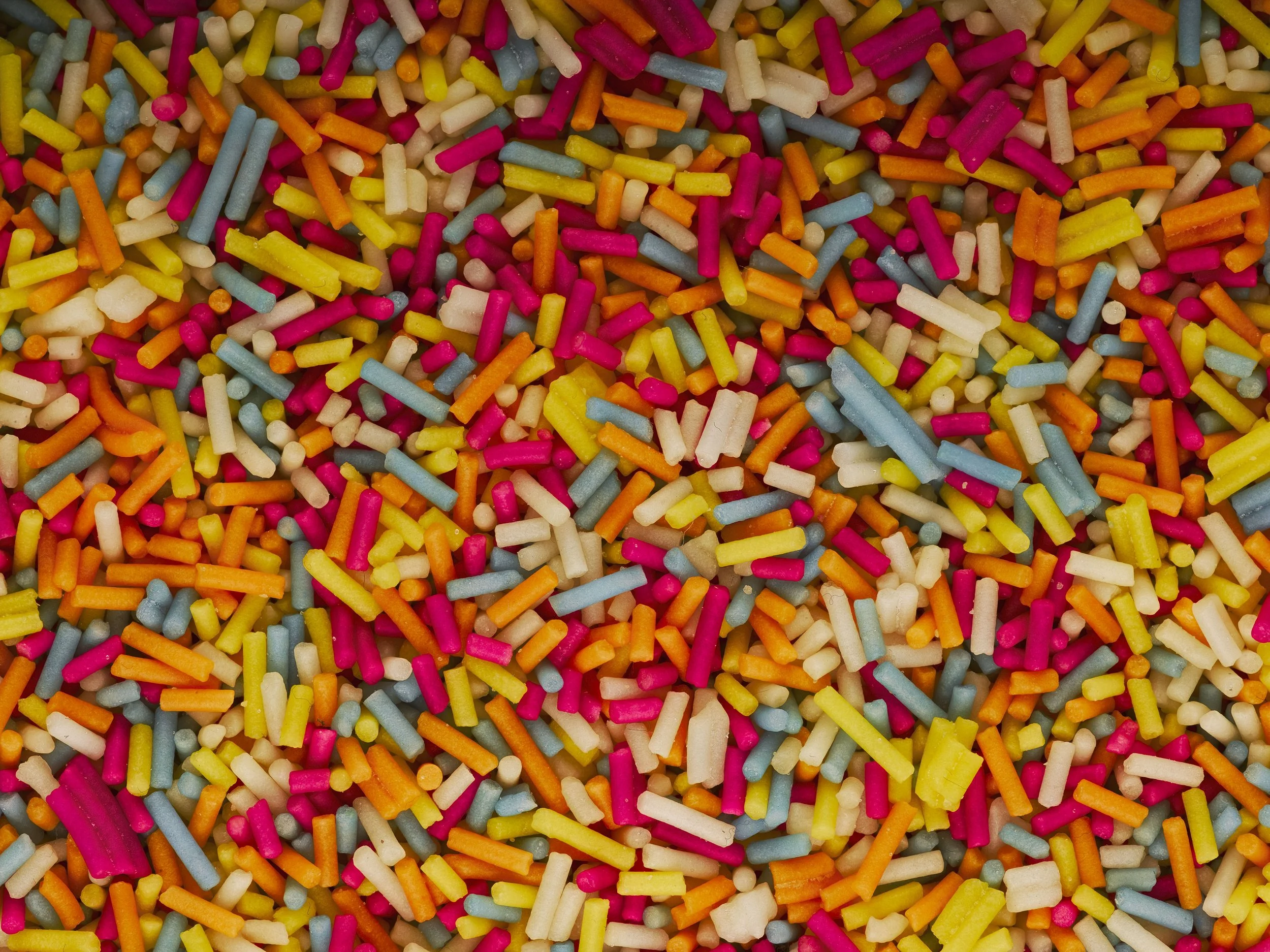 A close-up of colorful sprinkles, including pink, blue, white, yellow, orange, and green.