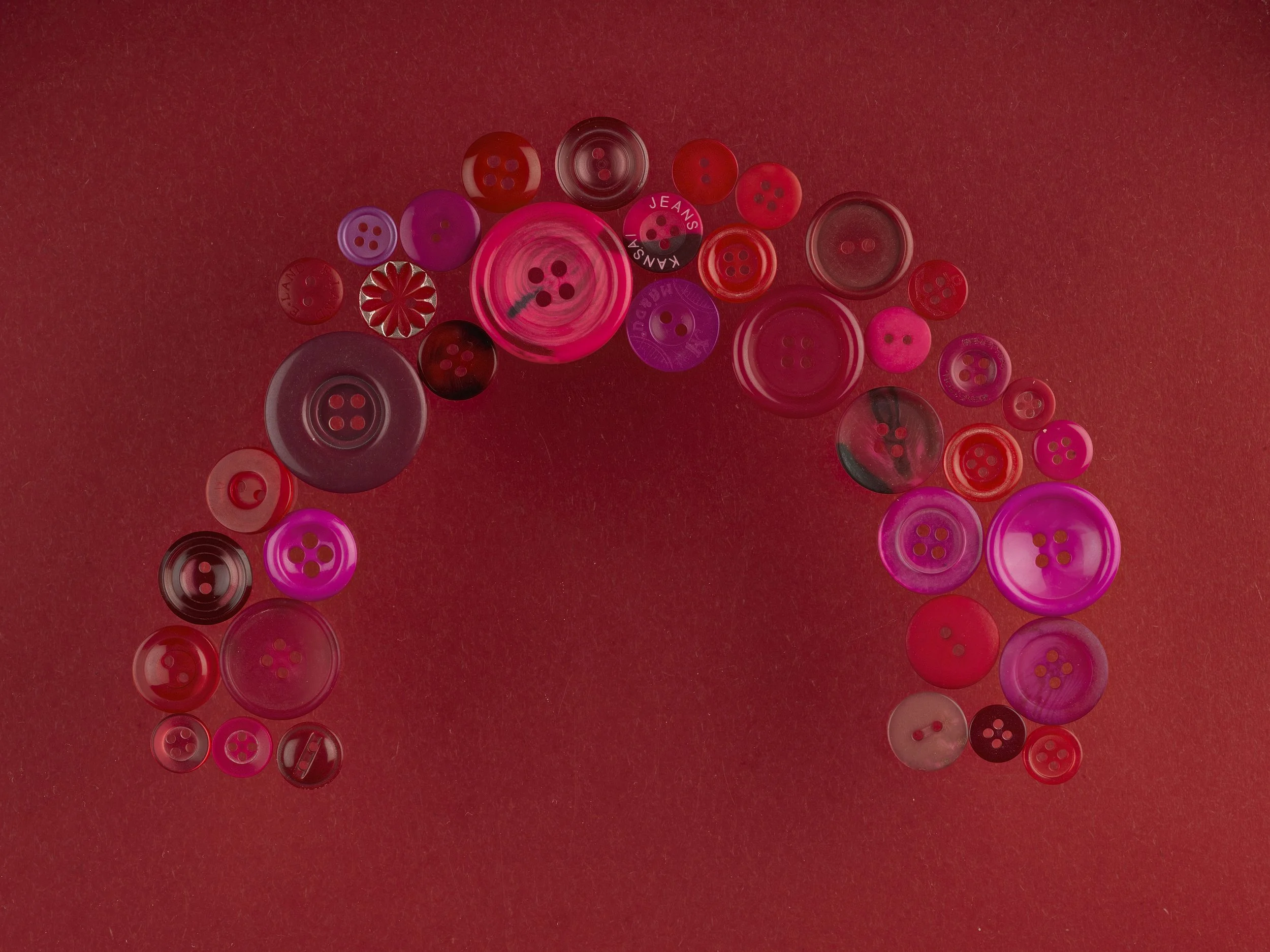 An arrangement of various red, pink, purple, and black buttons on a red background.