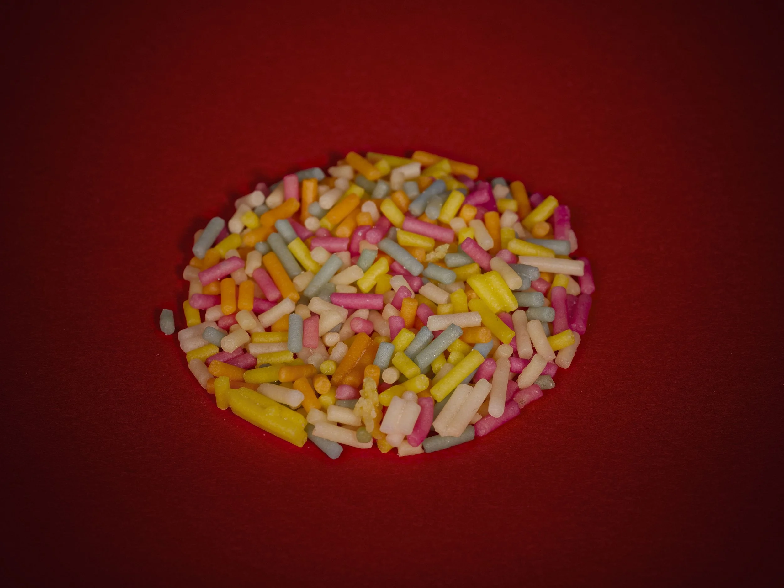 Colorful sugar sprinkles on a red surface.