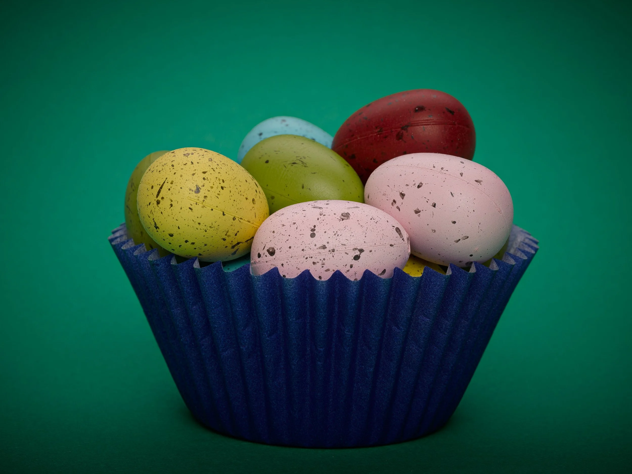 Colorful spotted eggs in a blue cupcake liner on a green background.