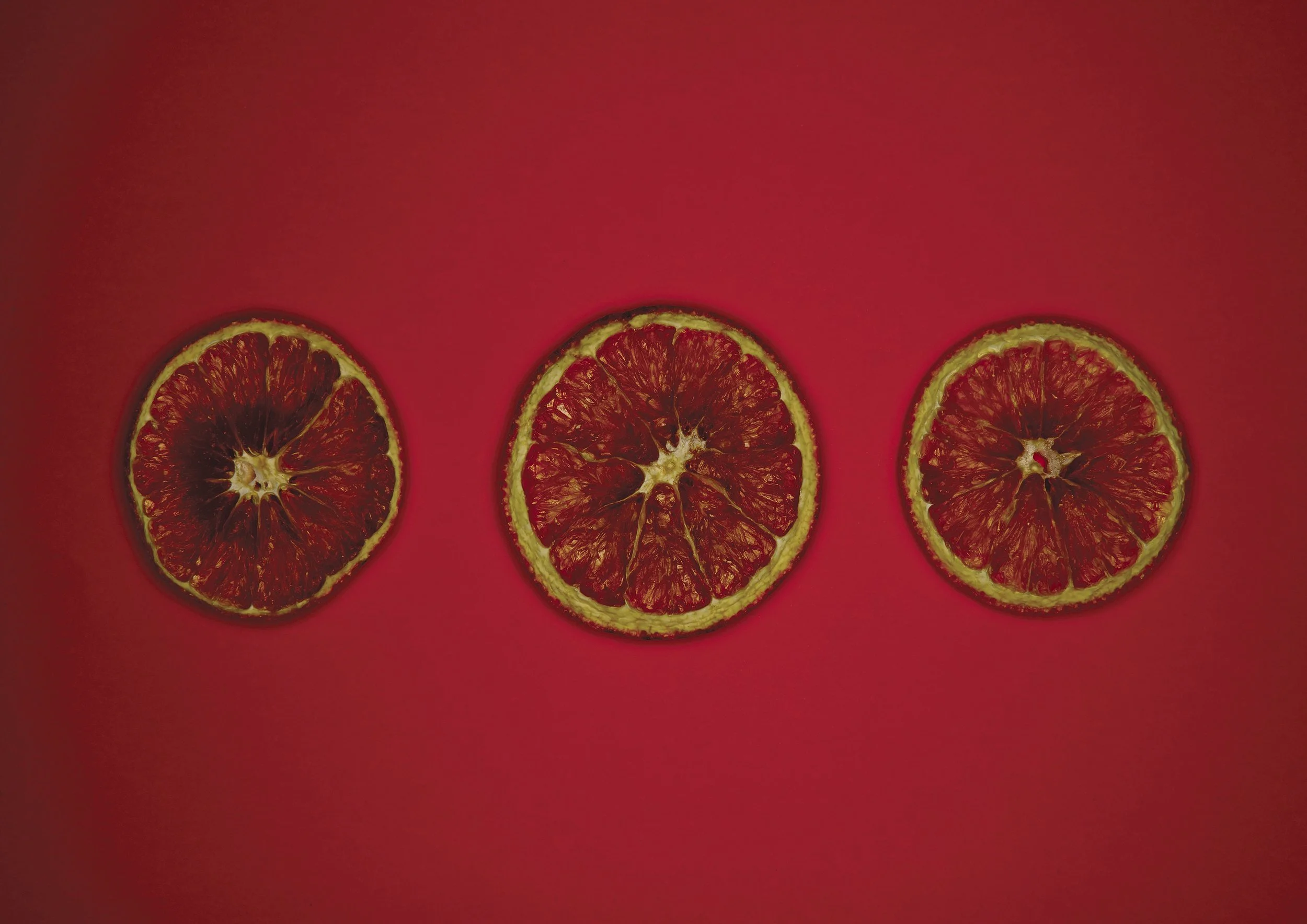 Three dried blood orange slices arranged in a row on a pink background.