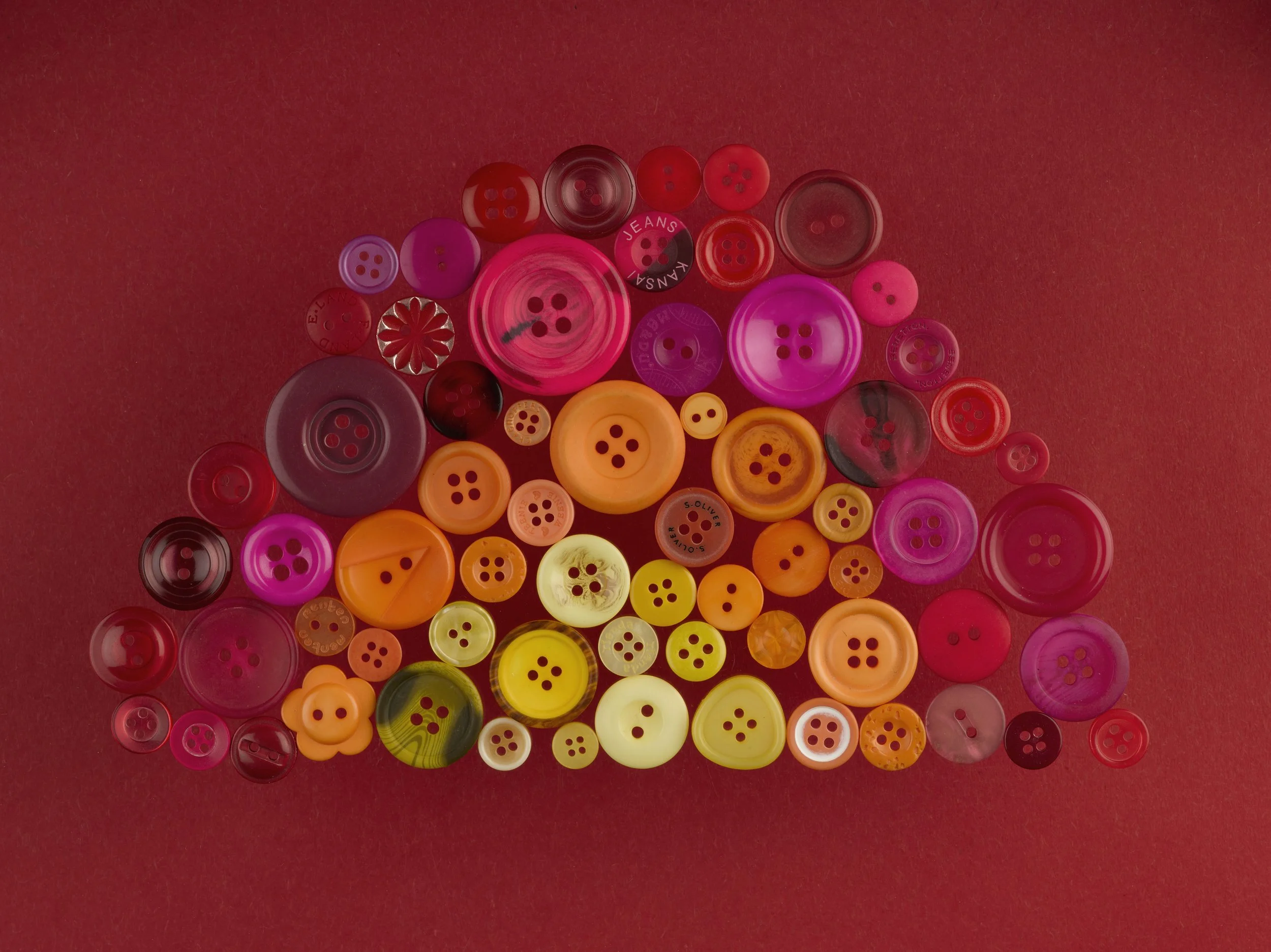 Collection of various colorful buttons on a reddish background.