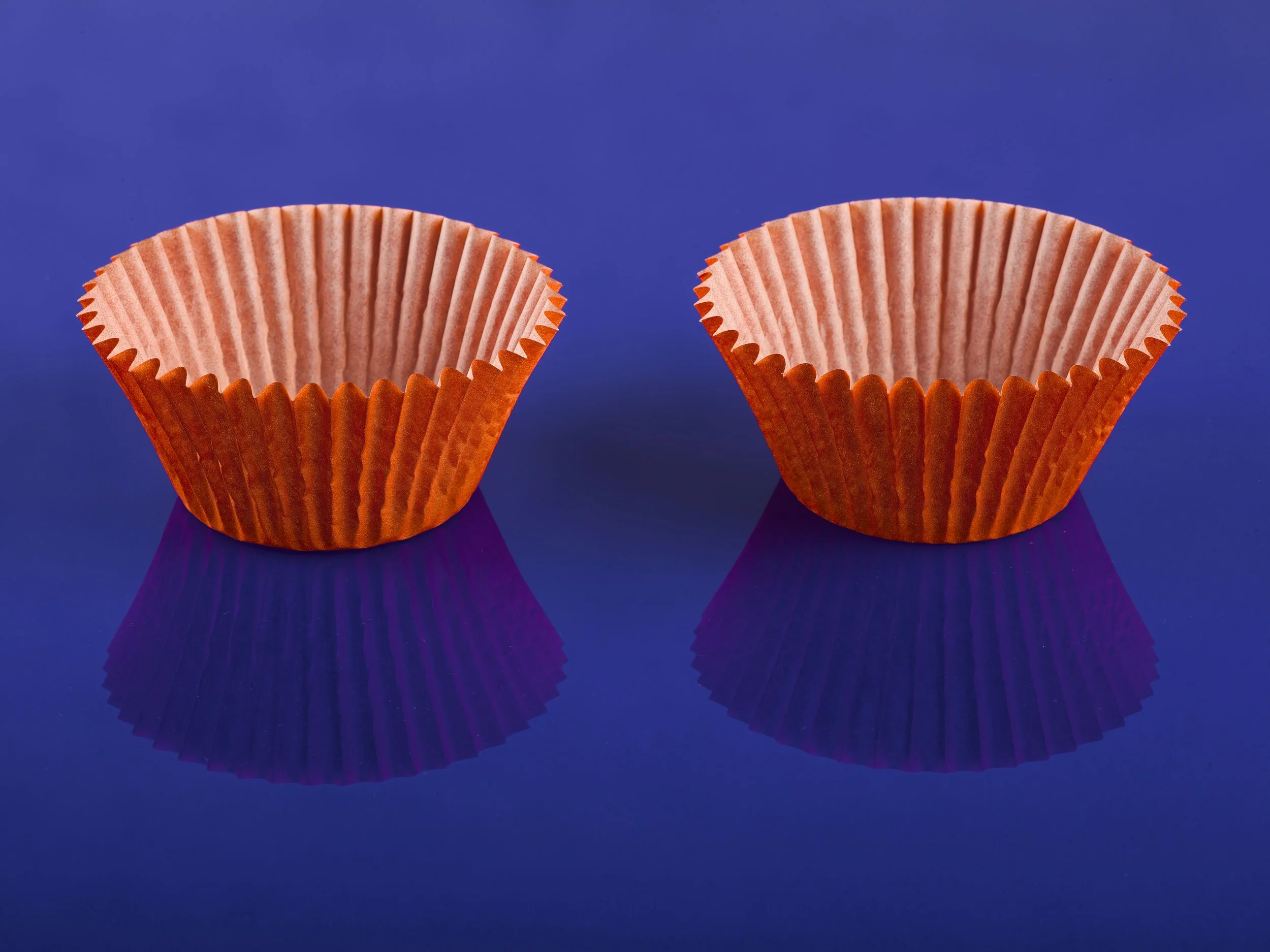 Two empty paper cupcake liners on a reflective purple surface.