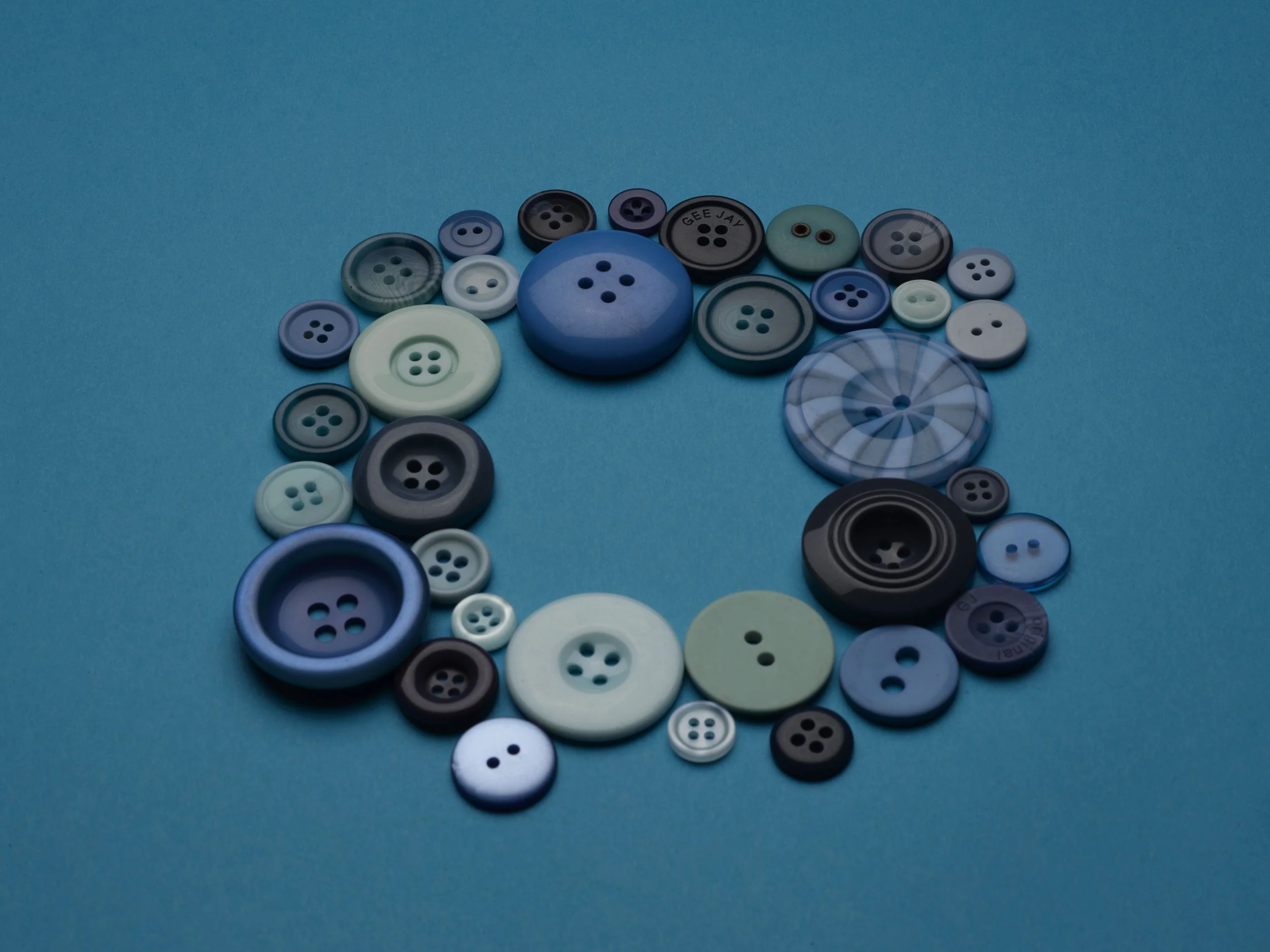 A collection of various blue, black, gray, white, and green buttons in different sizes arranged in a circle on a blue background.