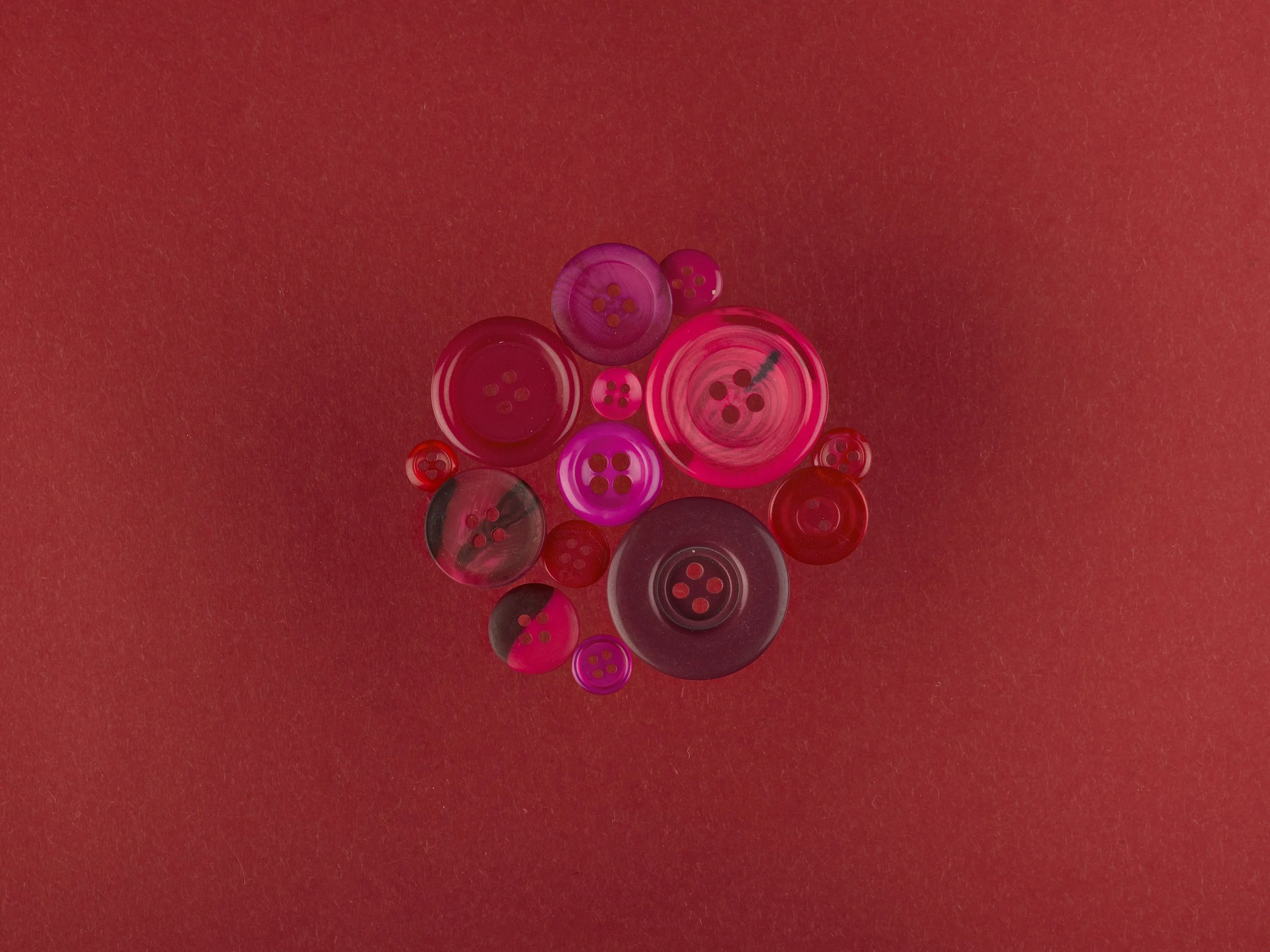 A collection of pink and red buttons of various sizes on a red textured background.