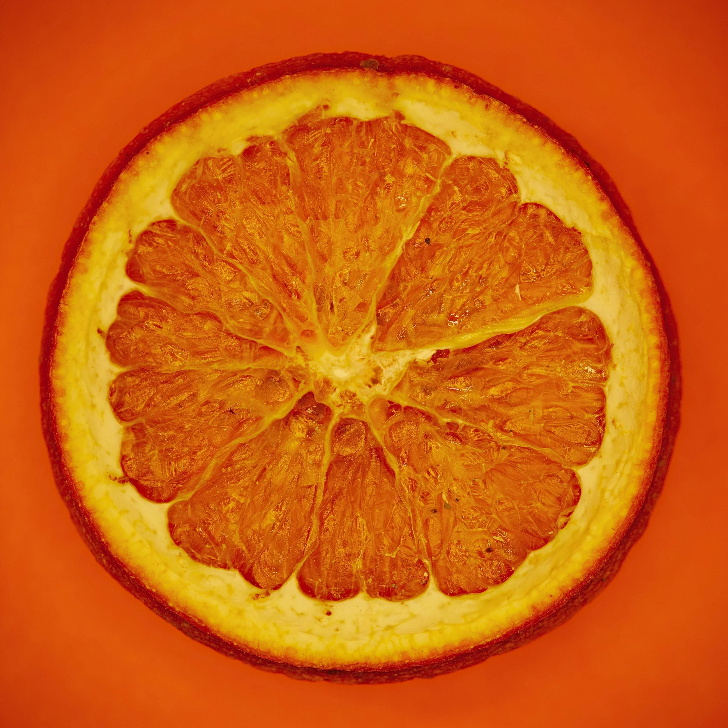A close-up of a sliced orange with its segments and inner texture visible, set against an orange background.