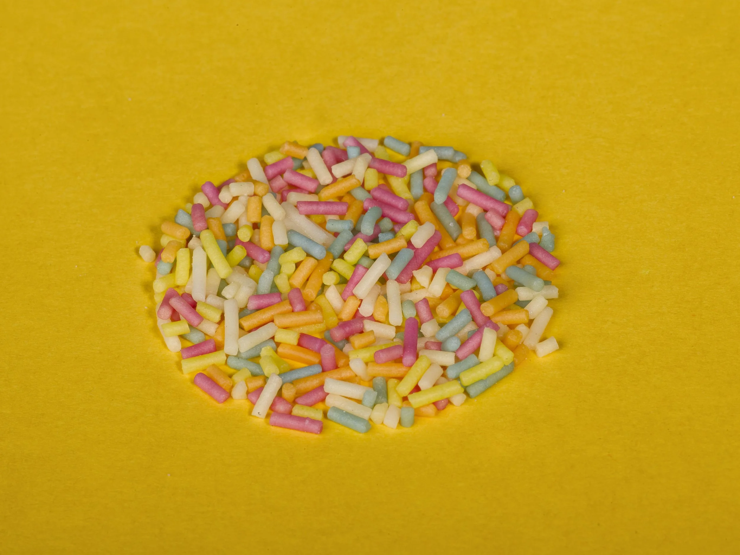 Small, colorful, pastel-colored candy sprinkles scattered on a yellow background.