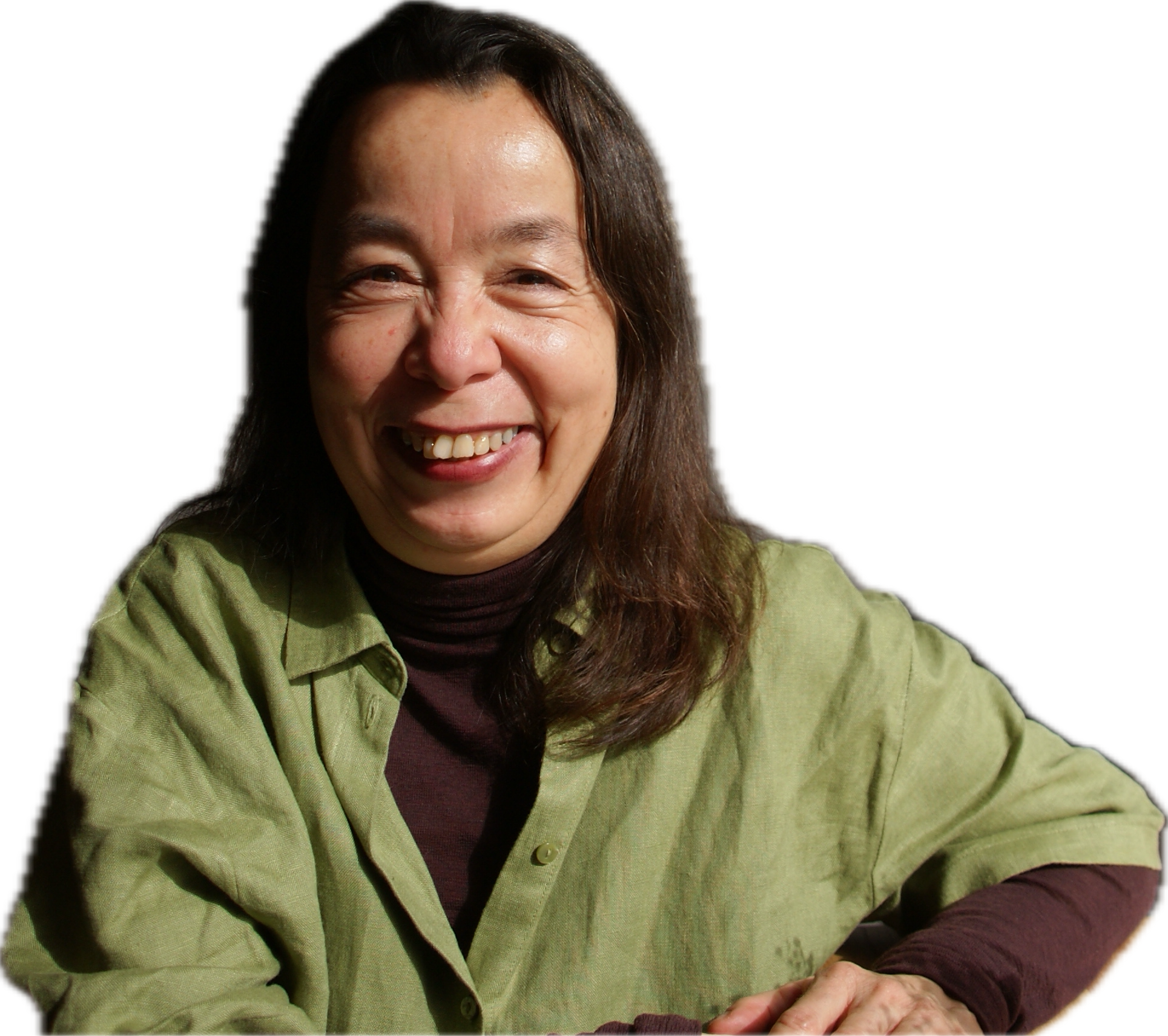 A woman with long dark hair smiling widely, wearing a green button-up shirt over a dark turtleneck, sitting with her arms resting on a surface against a black background.