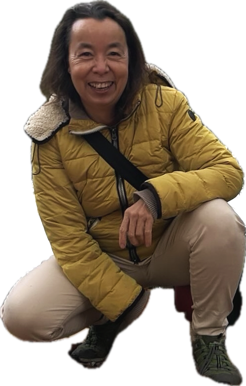 Woman in a yellow jacket and beige pants smiling and crouching.