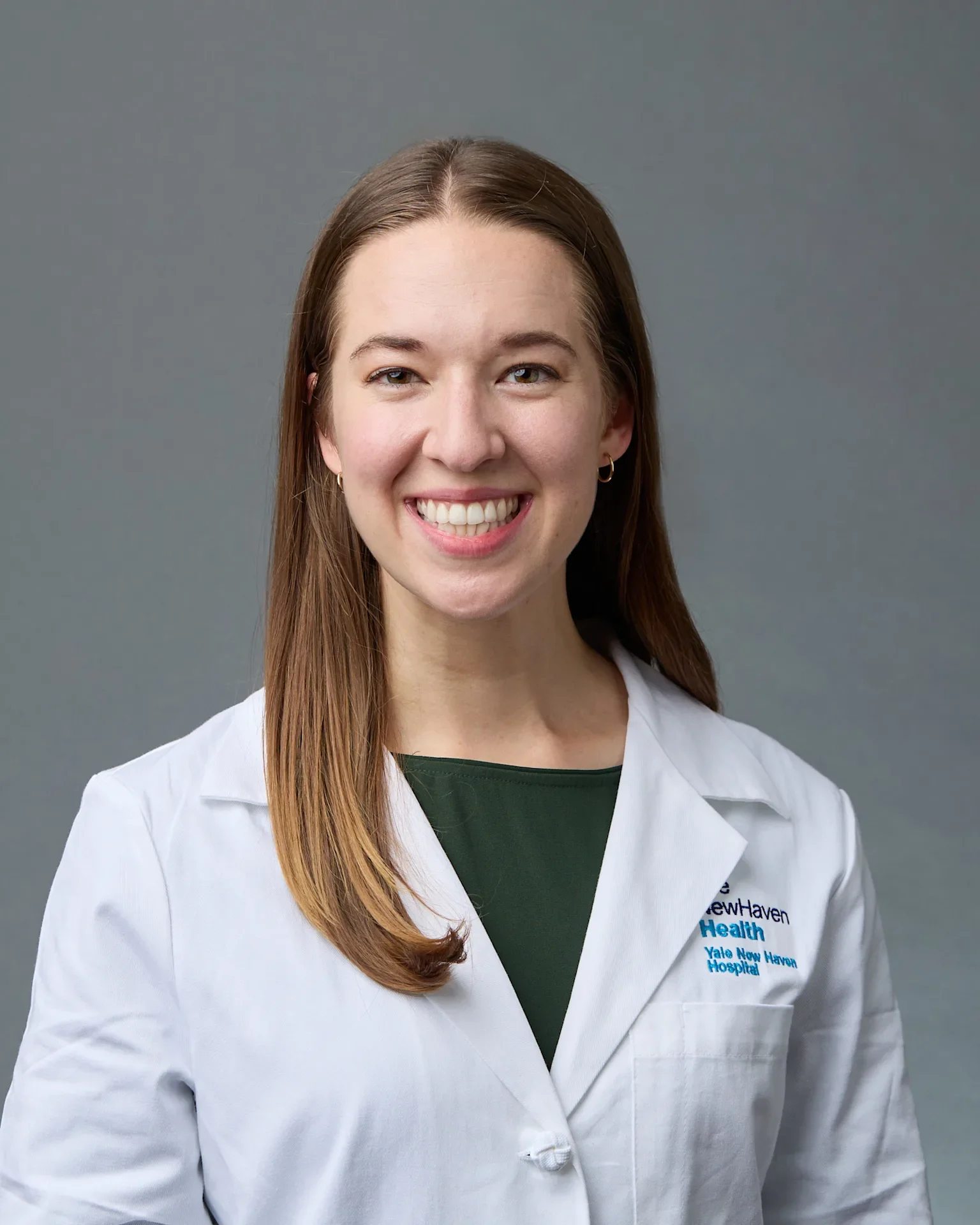 A smiling woman with long brown hair wearing a white coat with Yale New Haven Hospital logo.