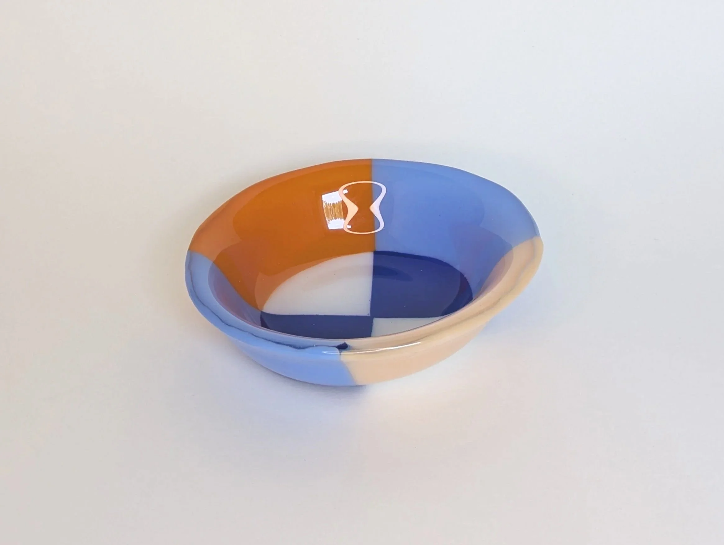 Circular glass bowl with geometric patterns in blue, orange, and white set on a plain light background.