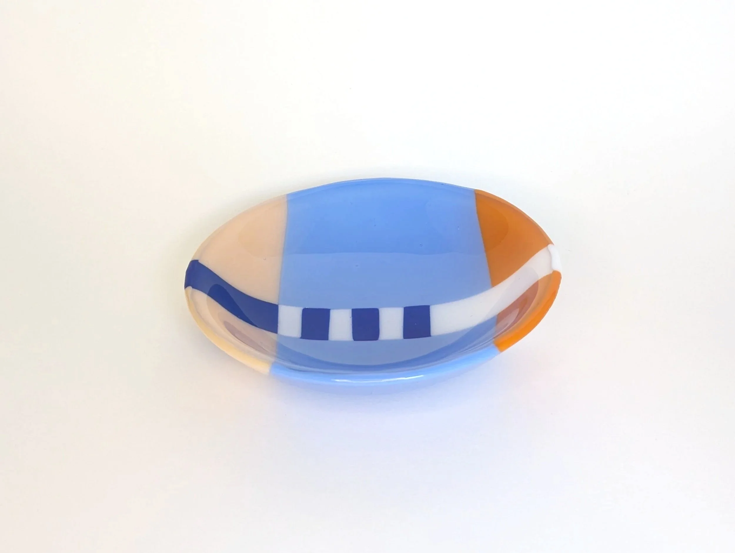 Circular glass bowl with geometric patterns in blue, orange, and white set on a plain light background.