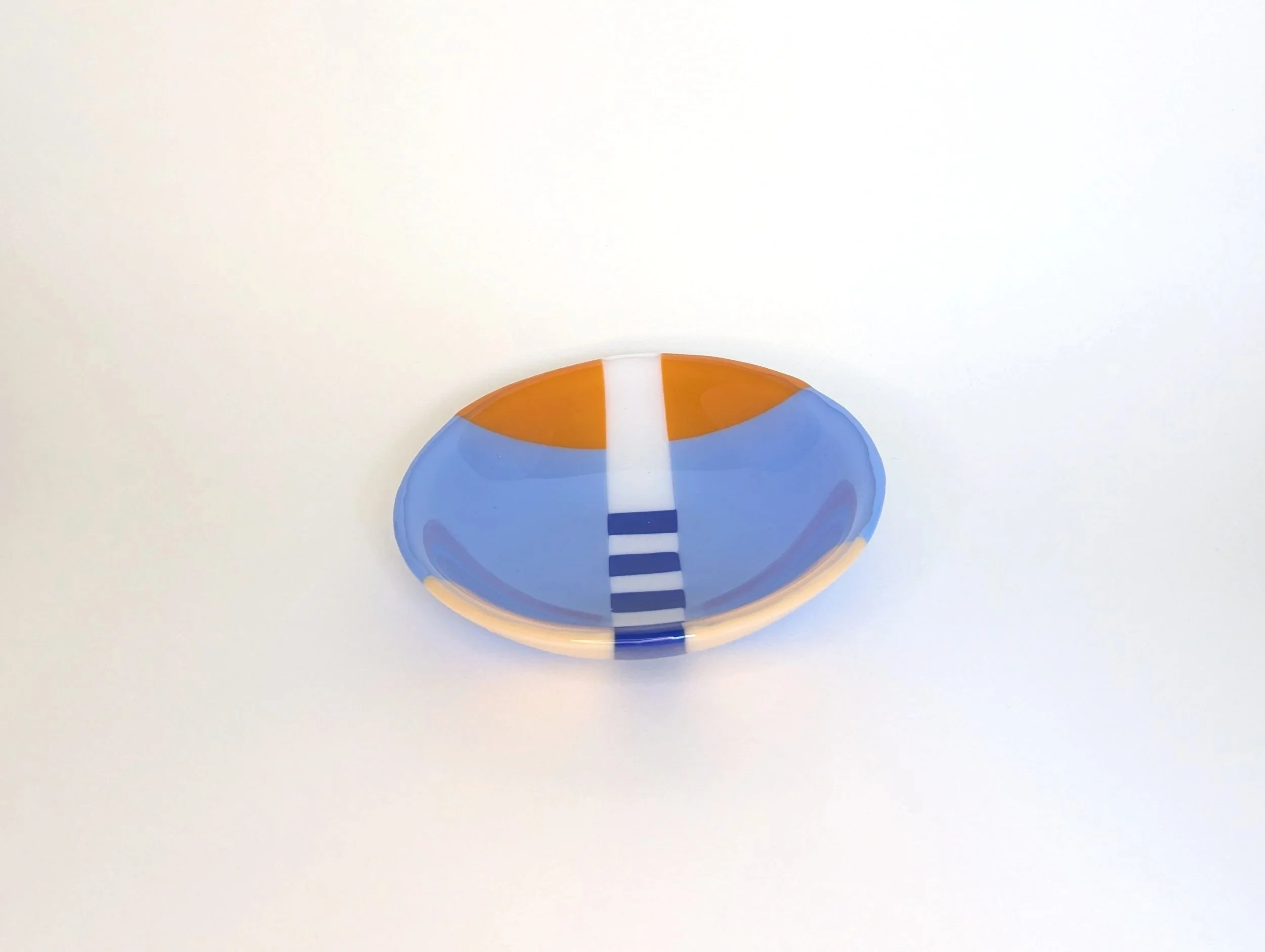 Circular glass bowl with geometric patterns in blue, orange, and white set on a plain light background.