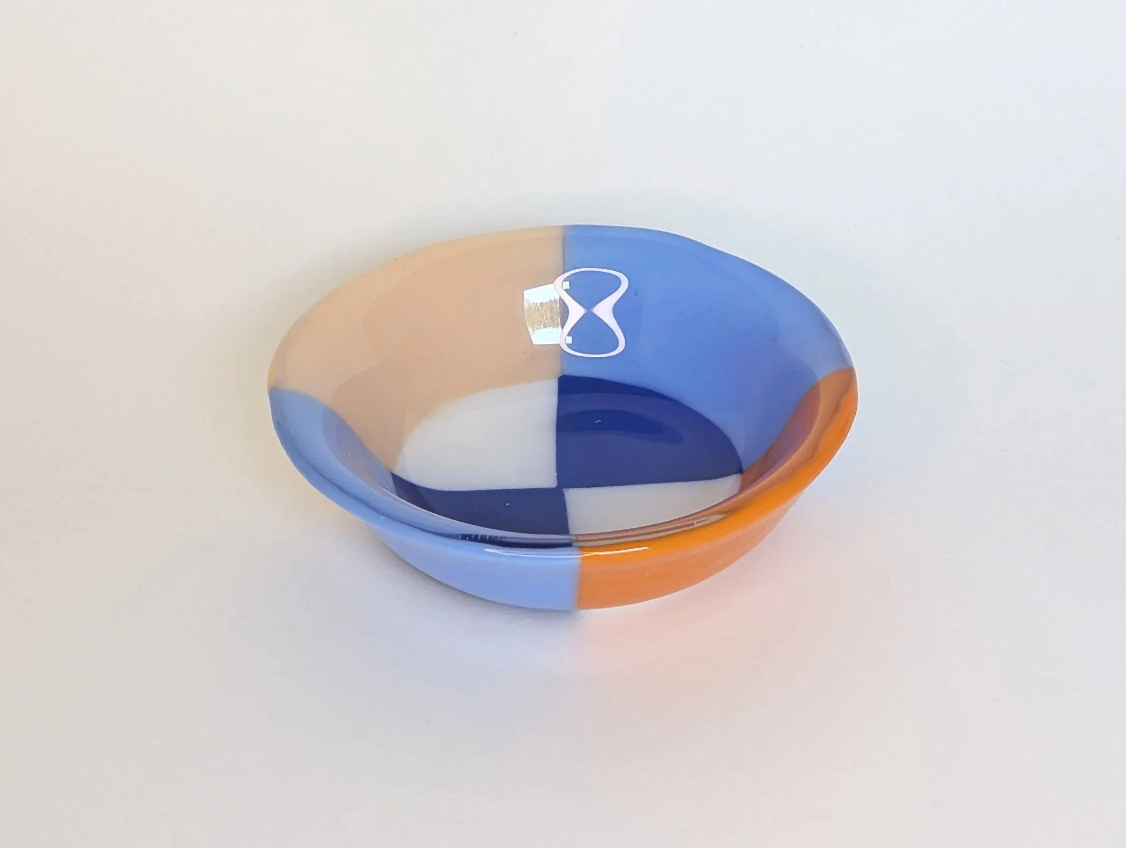 Circular glass bowl with geometric patterns in blue, orange, and white set on a plain light background.