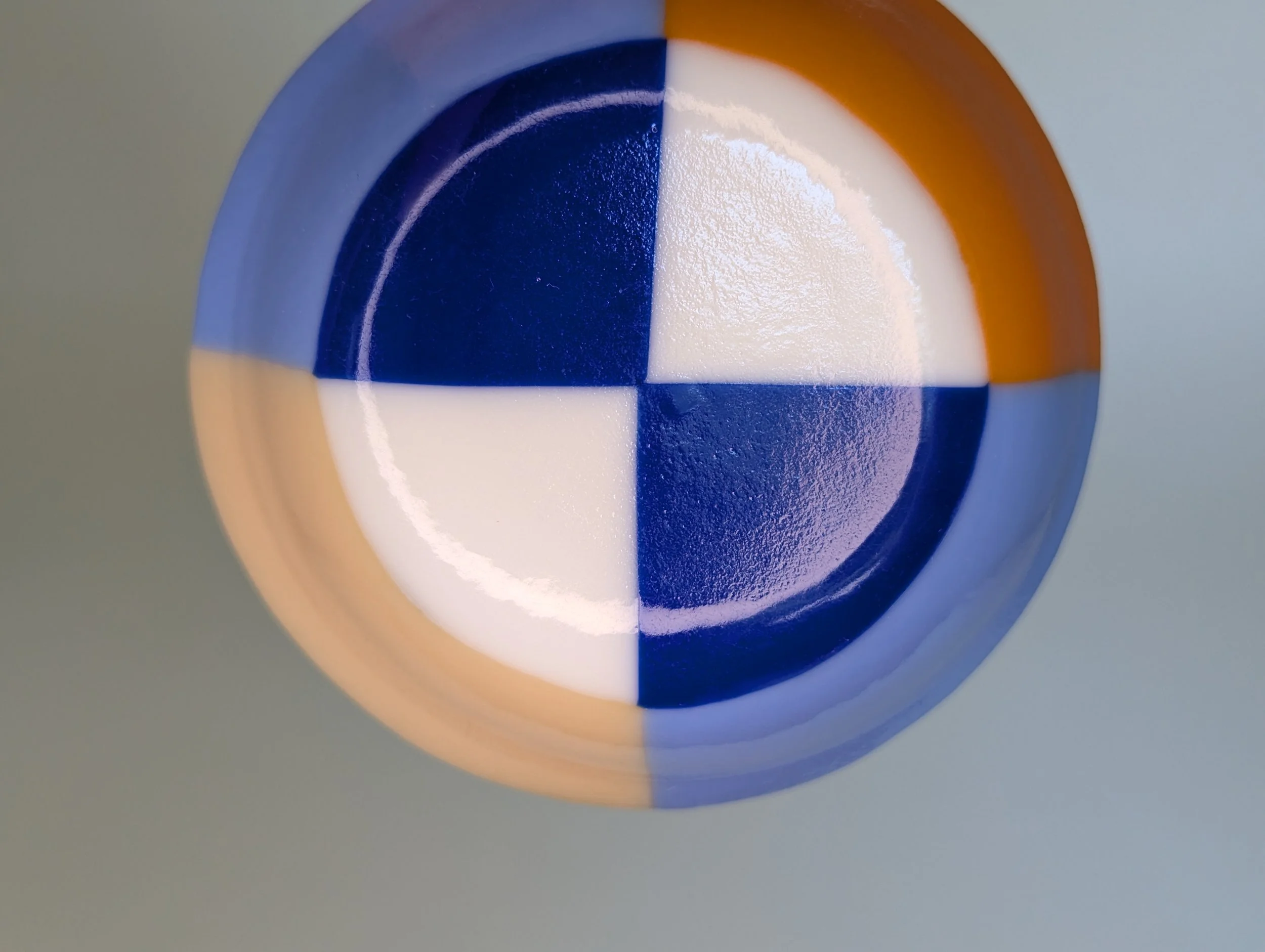 Circular glass bowl with geometric patterns in blue, orange, and white set on a plain light background.