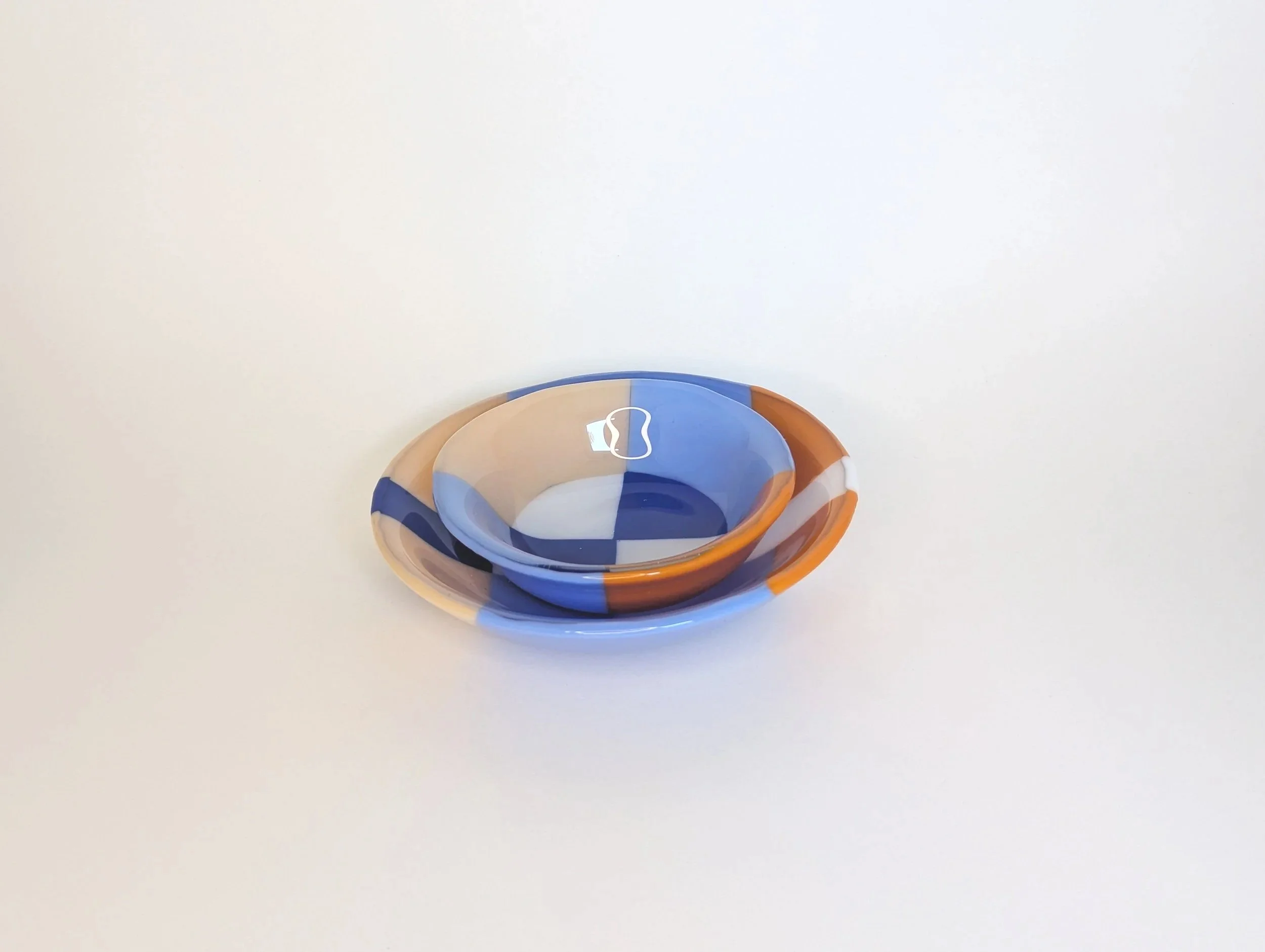 Two circular glass bowls with geometric patterns in blue, orange, and white set on a plain light background.