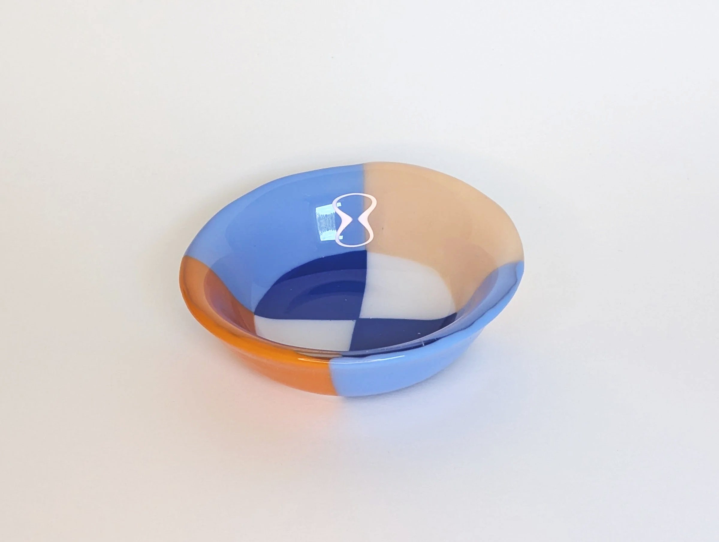 Circular glass bowl with geometric patterns in blue, orange, and white set on a plain light background.